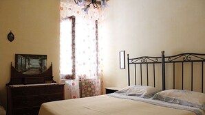 Une chambre à coucher avec un lit, une commode, un miroir et une fenêtre avec des rideaux.