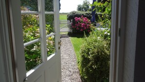 A garden view from a door with a white frame, gravel path, and a white picket fence. - Holidays by the sea in a historic thatched house: WiFi, 2 Smart TVs, sauna from 2022 (Pommerby)