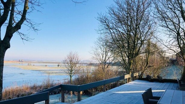 A wooden deck with a railing, overlooking a body of water and a distant landscape. - Vacation apartment in the Rosenhaus am See (Dagebüll)