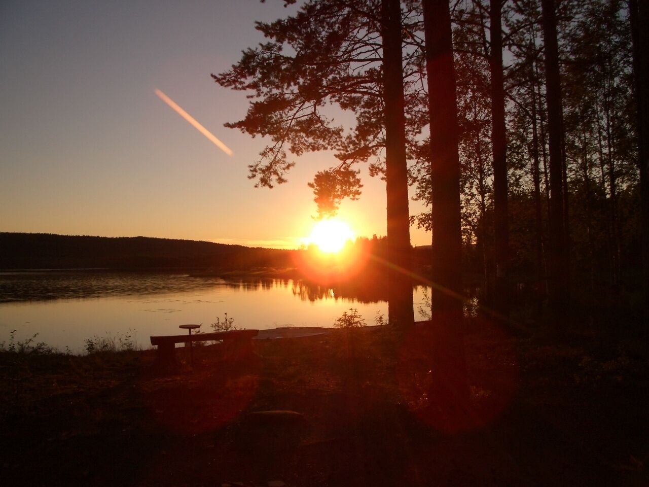 En solnedgång över en sjö med träd och en brygga.