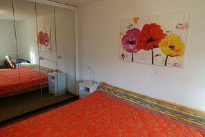 A bedroom with a bed, a nightstand, a mirror, and a wall with a floral painting. - Quiet & central–ideal starting point for swimmers & adventurous people (Tessin)