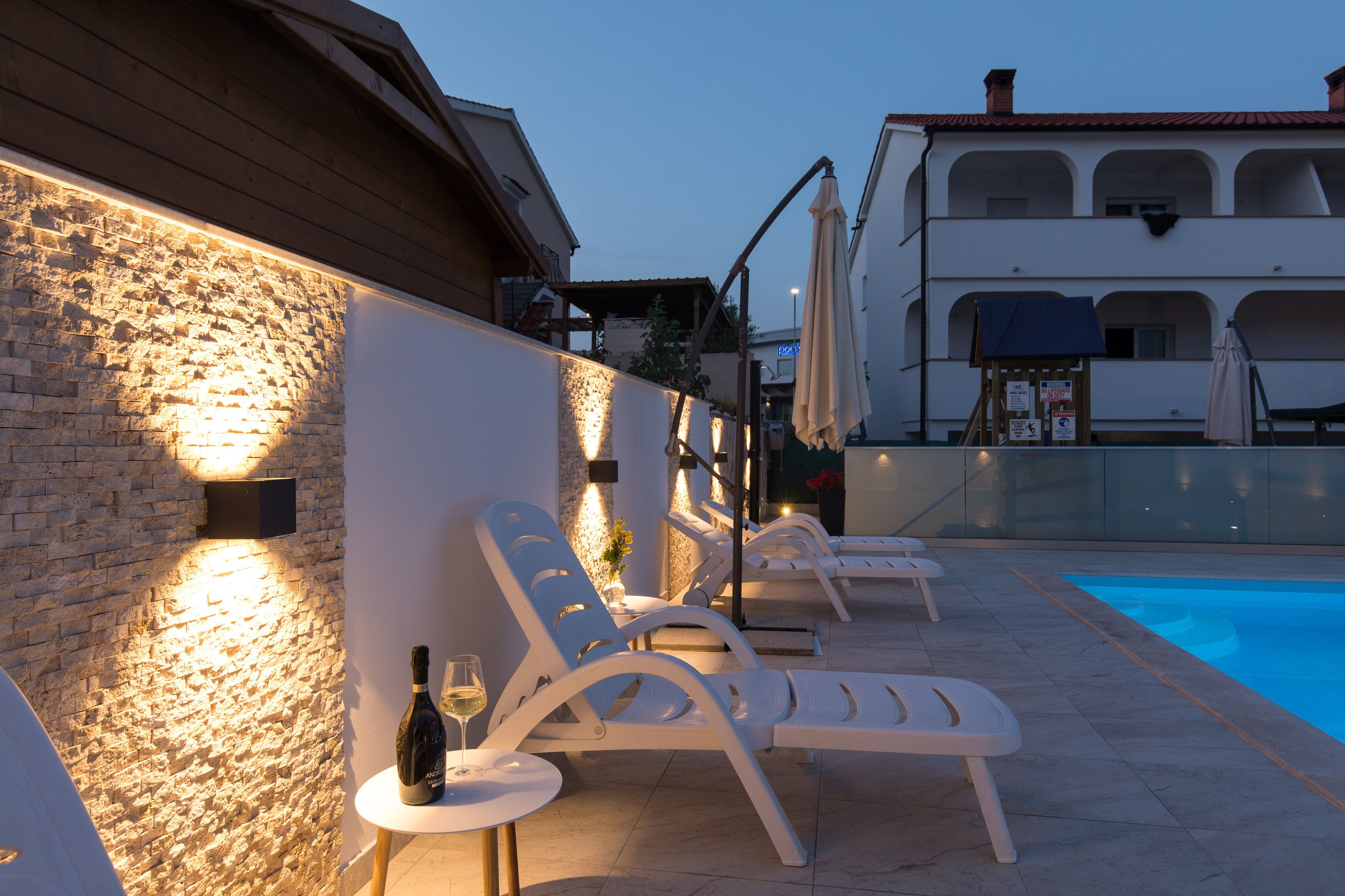 A poolside area with lounge chairs and a bottle of wine on a small table.