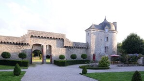 Un bâtiment historique en pierre, doté d’une cour intérieure, d’un chemin de gravier menant à l’entrée et de haies soigneusement taillées.