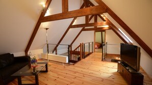 Une pièce de style « loft », avec des poutres en bois apparentes, une table basse en verre, un canapé, un téléviseur et un radiateur.