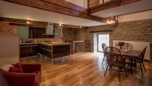 Une cuisine spacieuse avec des poutres en bois, un coin repas avec une table et des chaises, et un mur en pierre.