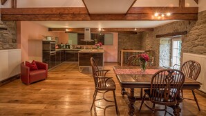 Un grand espace à manger avec une table et des chaises en bois, un canapé rouge et une cuisine en arrière-plan.