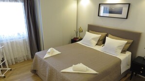 A neatly made bed with a beige bedspread and white pillows, a bedside table with a lamp, and a framed picture on the wall. - Modern apartment near the beach for 4 people (Trogir)