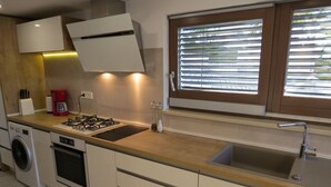 A modern kitchen with a built-in stove, oven, and washing machine, a window with blinds, and a sink. - Modern apartment near the beach for 4 people (Trogir)