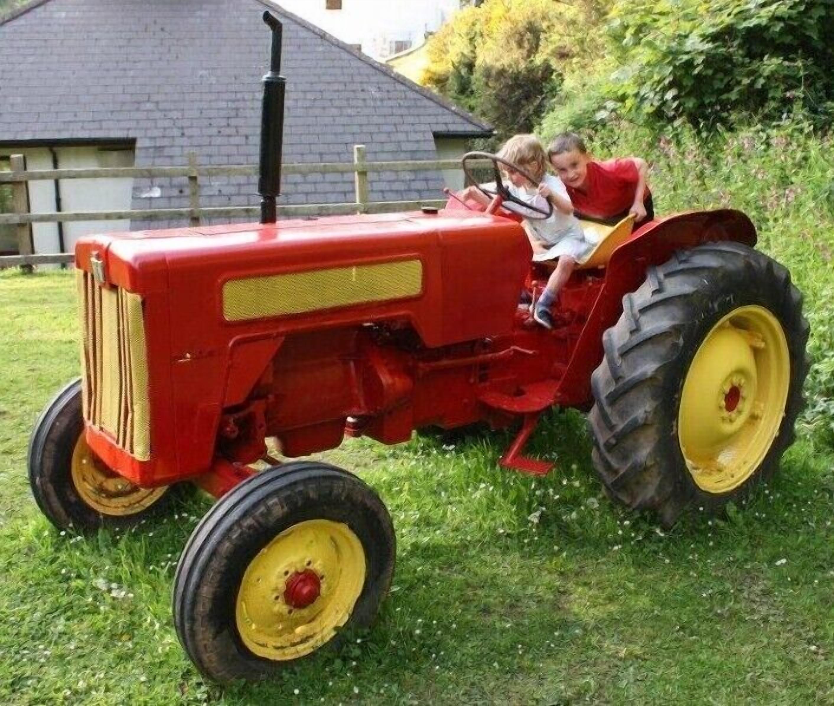 Un tracteur rouge sur lequel sont assis deux enfants.