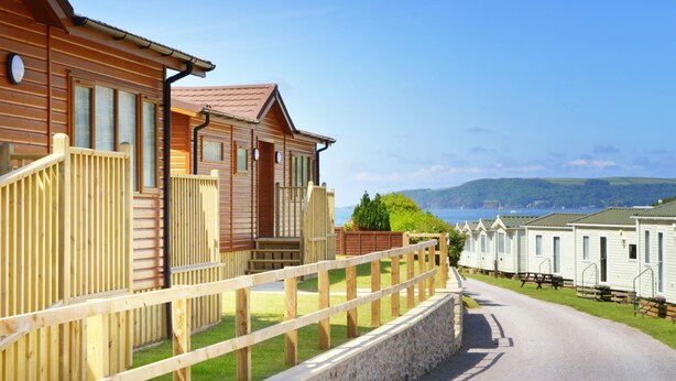 A row of wooden cabins with a stone wall and wooden fence in the foreground, and a clear view of the sea in the background. - 3 Bed Caravan, South Devon Coast nr Plymouth, 200m to Beach + Indoor Heated Pool (Nr Plymouth)