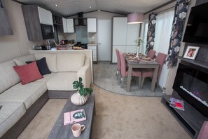Un espacio habitable compacto con sofá, mesa de centro, mesa de comedor y sillas. Se observa una zona de cocina al fondo.