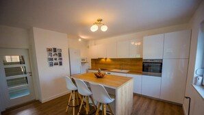 A modern kitchen with white cabinets, a wooden island with bar stools, and a built-in oven. - Luxury villa Vitam in Imotski, private pool (Zmijavci)