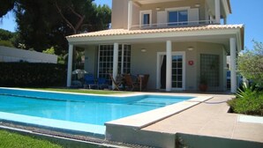 Una casa de dues plantes amb piscina, un porxo cobert amb cadires i un jardí.