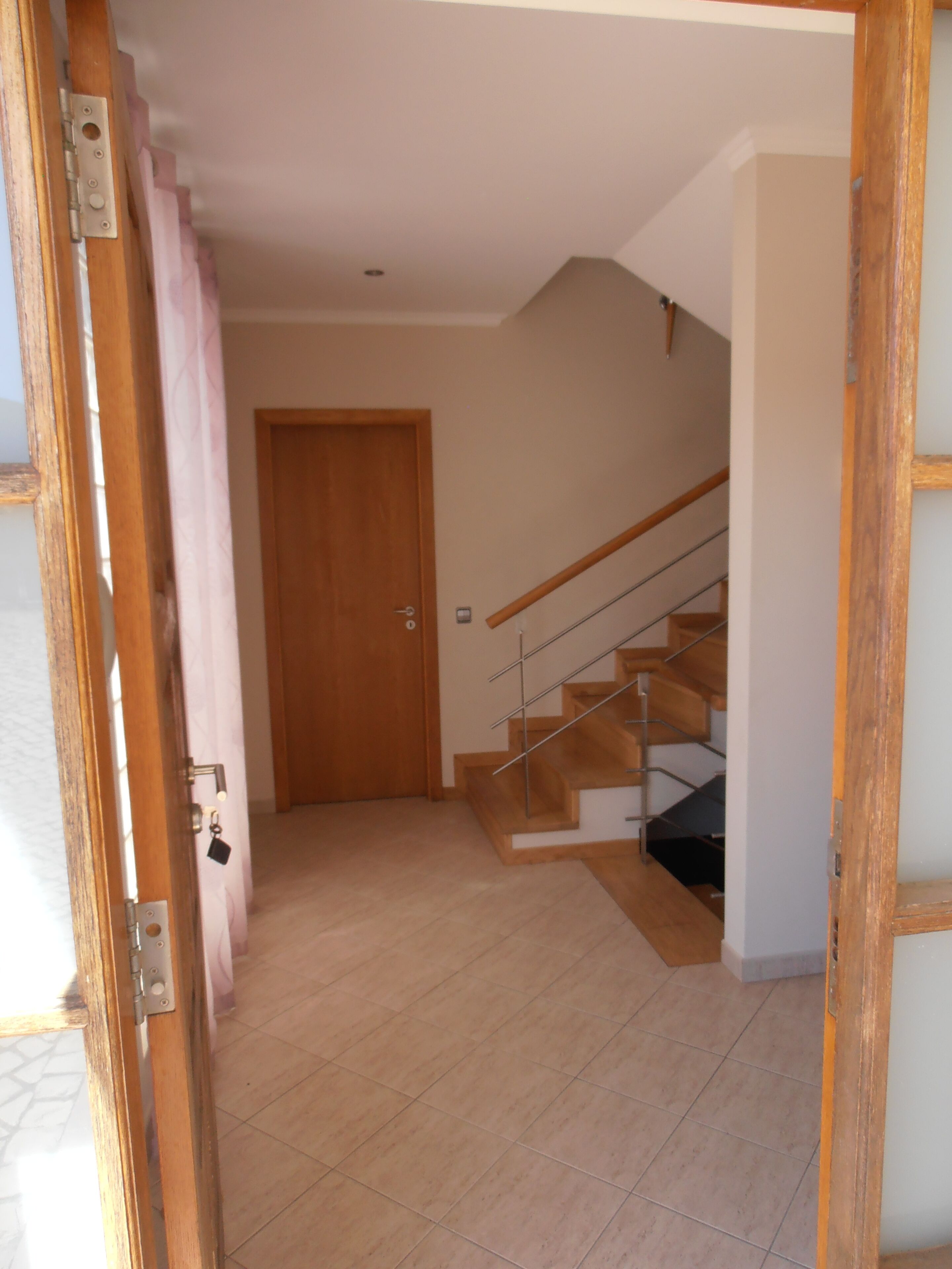 A hallway leading to a wooden door and a staircase with a handrail.