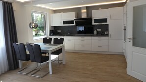 A modern kitchen with white cabinets, a black countertop, and a dining area with a table and chairs. - 5-star luxury apartment Albatros directly on the golf course with its own garage and terrace (Wiesmoor)