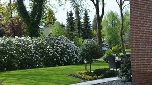 A well-maintained garden with a paved walkway, neatly trimmed grass, and flowering bushes. - 5-star luxury apartment Albatros directly on the golf course with its own garage and terrace (Wiesmoor)