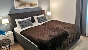 A neatly made bed with a dark headboard, two patterned pillows, and a brown blanket. A framed picture of a beach scene hangs above the bed. - 5-star luxury apartment Albatros directly on the golf course with its own garage and terrace (Wiesmoor)