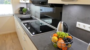 A modern kitchen with a built-in stove, a kettle, and a fruit bowl on the counter. - 5-star luxury apartment Albatros directly on the golf course with its own garage and terrace (Wiesmoor)