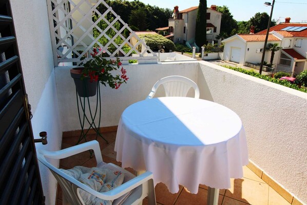 A small outdoor balcony with a white table and chair, a potted plant, and a white lattice structure.