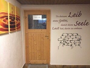 Eine Holztür mit einem Schild, auf dem "SAUMA" steht, und eine Wand mit einem Zitat auf Deutsch.