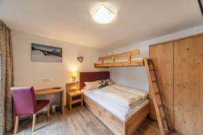 Ein kleines Schlafzimmer mit Etagenbett, Schreibtisch, Stuhl, Kleiderschrank und Nachttischlampe.