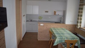 Una cocina compacta con armarios blancos, encimera de madera y zona de comedor con una mesa cubierta por un mantel escocés.