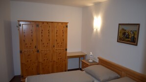 Un dormitorio con dos camas, un armario de madera, un escritorio y una mesita de noche.