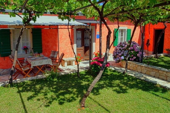 Un bâtiment rouge doté d’un patio couvert, de sièges en plein air et d’un jardin fleuri.