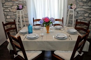 A dining table set for four with white plates, silverware, and a vase of flowers.