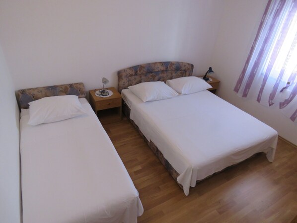 A room with two single beds, wooden nightstands, a lamp, and a window with curtains.