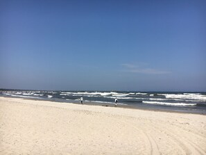 Una extensa playa de arena con olas suaves y un cielo azul despejado.