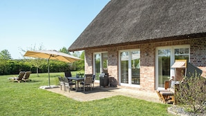 A brick house with a thatched roof, a patio with outdoor furniture, and a grill.