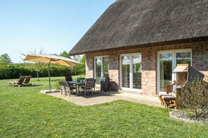 Una casa de ladrillo con tejado de paja, un patio con mobiliario exterior y una parrilla.