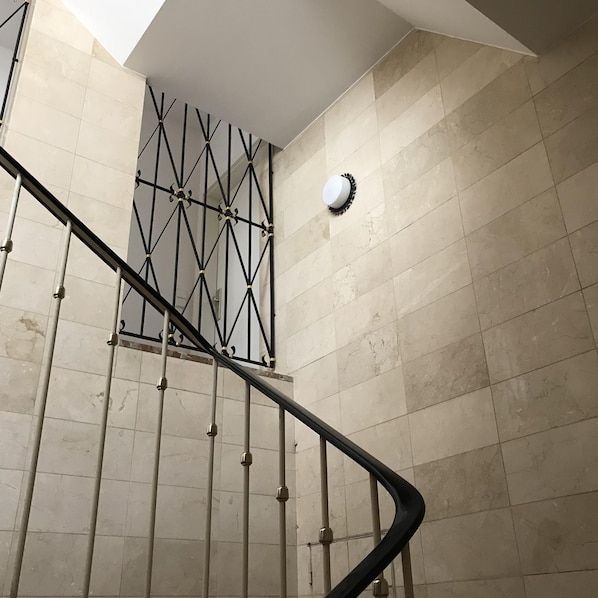 A staircase with a metal railing, beige tiled walls, and a ceiling light fixture.