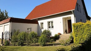 Kaksikerroksinen talo, jossa on punatiilinen katto, valkoiset ulkoseinät ja pieni kuisti.
