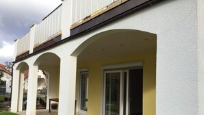 En bygning med gul facade, hvide søjler og en overdækket terrasse med glasdøre.