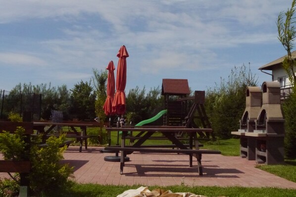 A playground with slides and swings, picnic tables, and red umbrellas. - Family-friendly, green area, barbecue area, surrounded by pastures, nature park (Rowy)