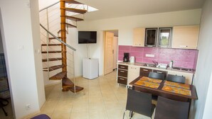 A compact kitchen with a built-in stove, a dining table with chairs, and a staircase with a TV mounted above it. - Family-friendly, green area, barbecue area, surrounded by pastures, nature park  (Rowy)