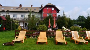 A building with a red and white facade, a balcony with a wooden railing, and a lawn with four lounge chairs. - Family-friendly, green area, barbecue area, surrounded by pastures, nature park  (Rowy)