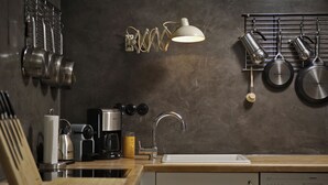 Una cucina moderna con piano di lavoro in legno, una macchina da caffè, un bollitore e un espositore a sospensione per pentole.
