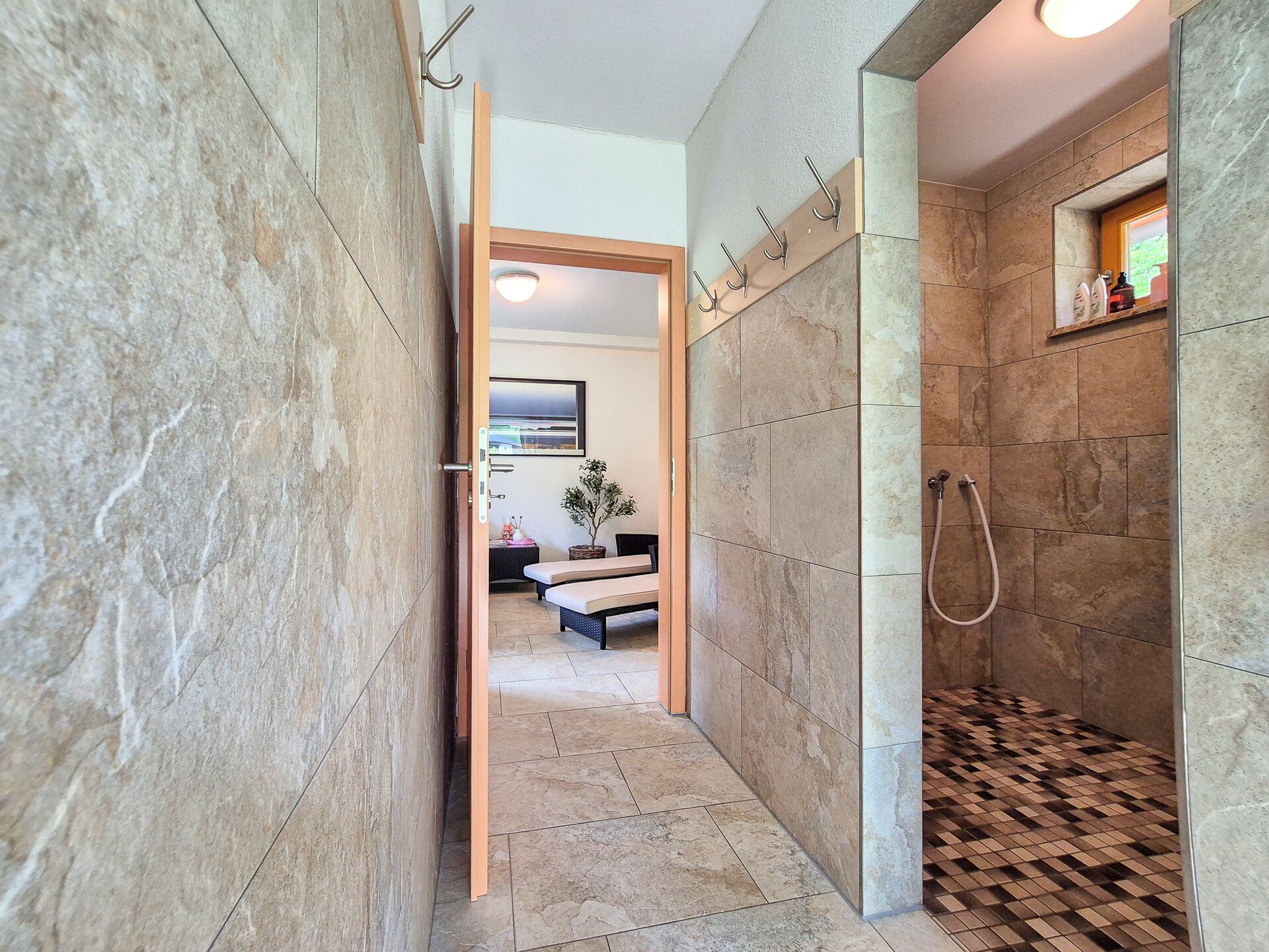 A modern bathroom with a shower, a towel rack, and a view into a living area.