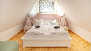 Un llit doble ben fet amb roba de llit blanca i almoades, una tauleta de nit i una finestra amb cortina floral.