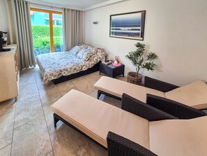 A hotel room with a bed, a sofa, a small table, a potted plant, and a painting on the wall.