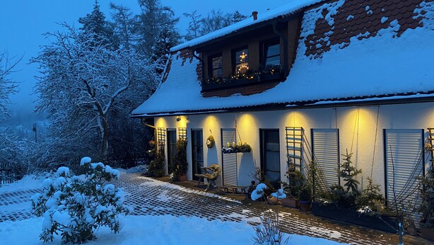 Una casa cubierta de nieve con techo inclinado, un balcón con luces de cuerda y una entrada bien iluminada.