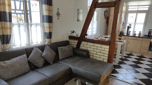 A living room with a grey sofa, a glass coffee table, and a kitchen in the background.