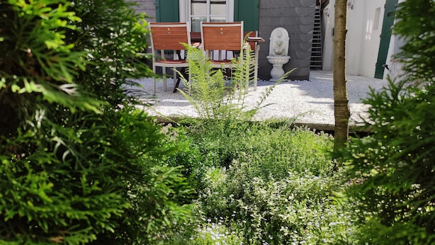 A garden with a table and chairs, surrounded by greenery and a stone sculpture.