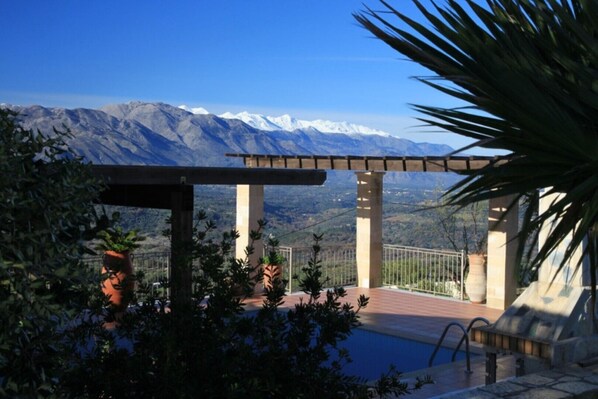 Un espace piscine agrémenté d’une pergola, de plantes en pot et offrant une vue sur des montagnes enneigées.
