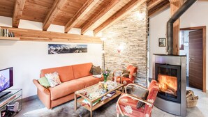 A cozy living room with a wooden ceiling, a stone wall, a fireplace, a sofa, and a television.
