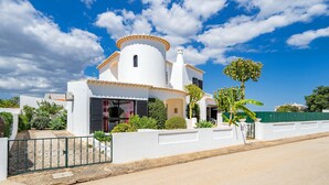 Una villa blanca con techo curvo, rodeada de follaje y un cielo azul despejado.