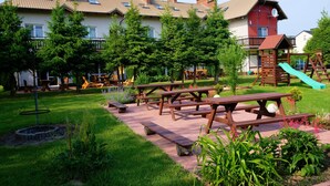 Un patio con mesas de picnic, juegos infantiles y un edificio de fachada roja.